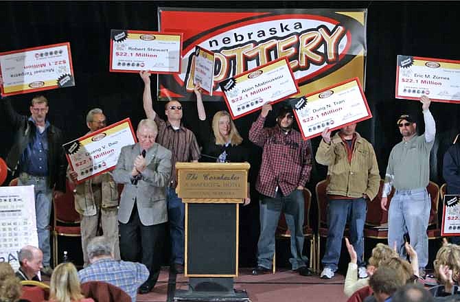 In this Feb. 22, 2006, file photo, the eight winners of the $365 million Nebraska Powerball lottery hold up their ceremonial checks at a news conference in Lincoln, Neb. Reacting to the drawing for a $500 million Powerball jackpot this week, past winners of mega-lottery drawings and financial planners have some advice: stick to a budget, invest wisely, learn to say no and be prepared to lose friends while riding an emotional roller-coaster.