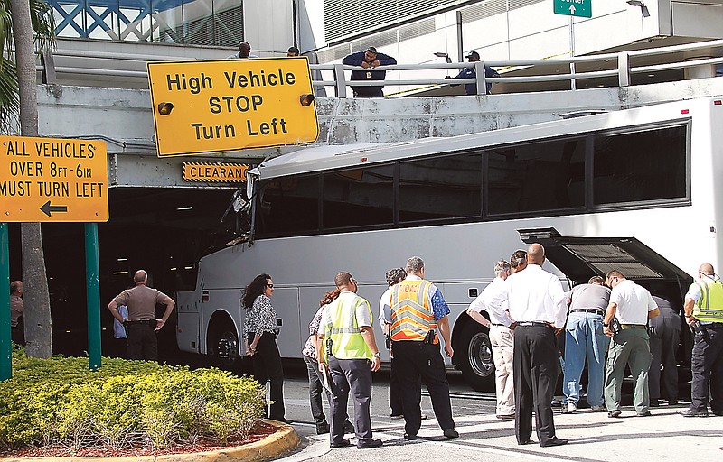 Workers and law enforcement officers prepare to remove a bus after it hit a concrete overpass at Miami International Airport in Miami on Saturday. The vehicle was too tall for the 8-foot-6-inch entrance to the arrivals area, and buses are supposed to go through the departures area which has a higher ceiling.
