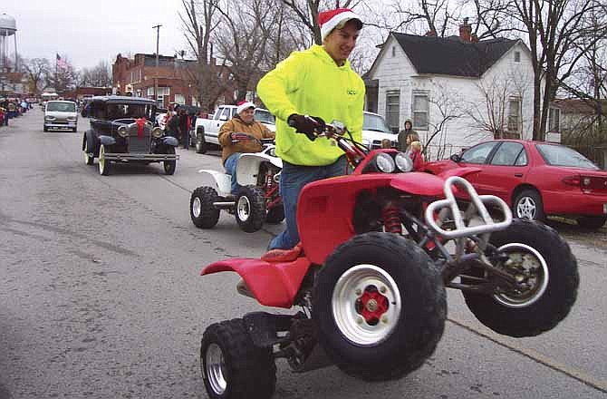 Taylor Zumwalt pops a wheelie on his four-wheeler Saturday at the Russellville Christmas Parade while Tyler Strauch revs the engine of his white four-wheeler.