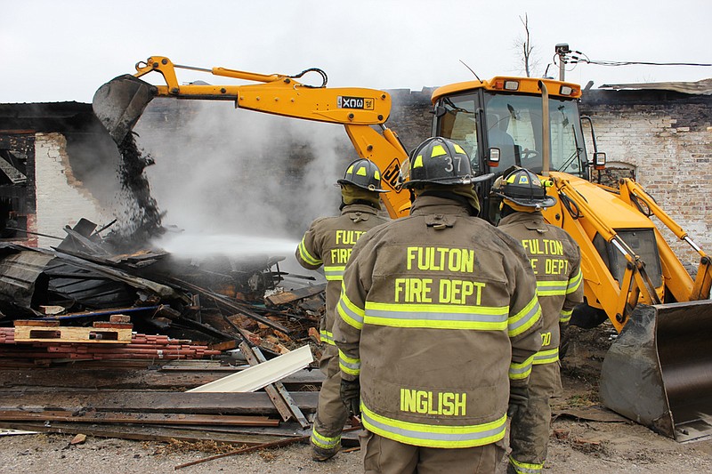 A City of Fulton worker uses a backhoe to dig out tin roofing while Fulton Fire Department officials blast the seat of the fire Monday at Nelson's Garage. Fulton Fire also had help from Central Callaway Fire District and Columbia Fire Department.