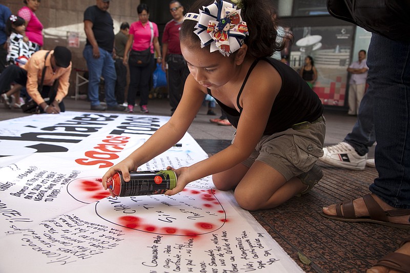 A young girl spraypaints red dots on her message of encouragement for Venezuela's President Hugo Chavez, outlined with a heart on a giant poster in Caracas, Venezuela, Friday. Somber confidants of Chavez say he is going through a difficult recovery after cancer surgery in Cuba. 