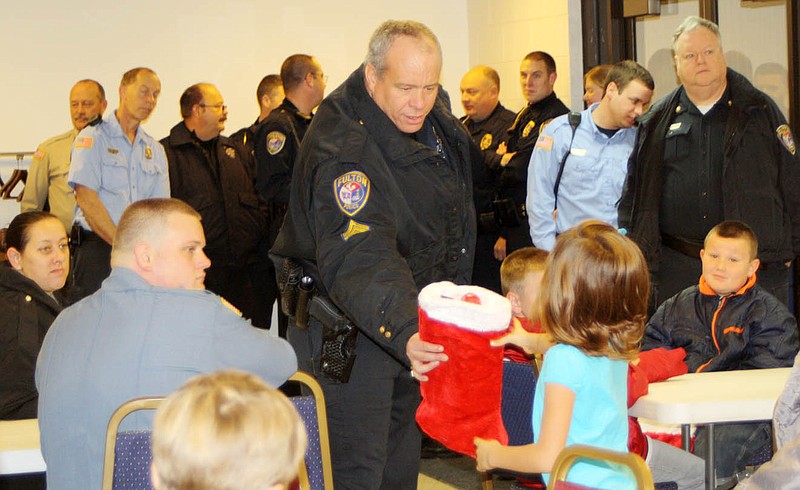 Sgt. Joe Schramm of the Fulton Police Department hands a Christmas stocking from the Dollar General Distribution Center in Fulton to one of the Callaway County youngsters participating in the annual Shop With A Cop Day in Fulton early Saturday morning. Each youngster received gift cards and gifts worth a total of about $175 at the Fulton Police Station that they used to shop for themselves and their families at Walmart.