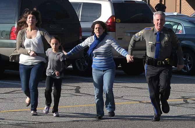 In this photo provided by the Newtown Bee, a police officer leads two women and a child from Sandy Hook Elementary School in Newtown, Conn., where a gunman opened fire, killing 26 people, including 20 children, Friday, Dec. 14, 2012. (AP Photo/Newtown Bee, Shannon Hicks) 