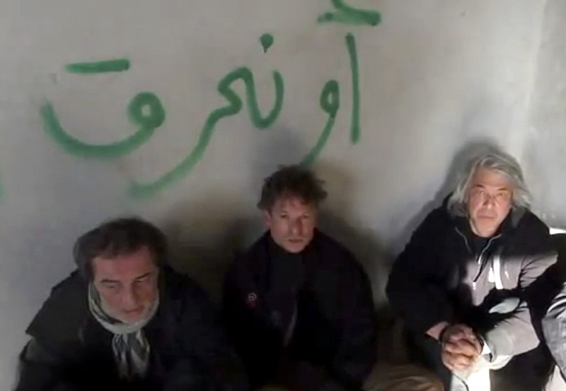 This image taken from undated amateur video posted on the Internet shows NBC chief foreign correspondent Richard Engel, center, with an unidentified Turkish colleague, left, and NBC photographer John Kooistra, right, after they were taken hostage in Syria for five days. They finally escaped unharmed during a firefight between their captors and anti-regime rebels, Engel said Tuesday. The Arabic writing on the wall reads, "or we will burn."