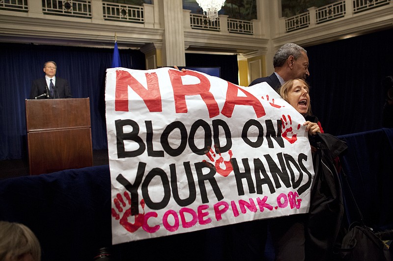 Activist Medea Benjamin, of Code Pink, is led away by security as she protests during a Washington statement by National Rifle Association executive vice president Wayne LaPierre, left, during a news conference Friday in response to the Connecticut school shooting. The National Rifle Association broke its silence Friday on last week's shooting rampage at a Connecticut elementary school, that left 26 children and staff dead.