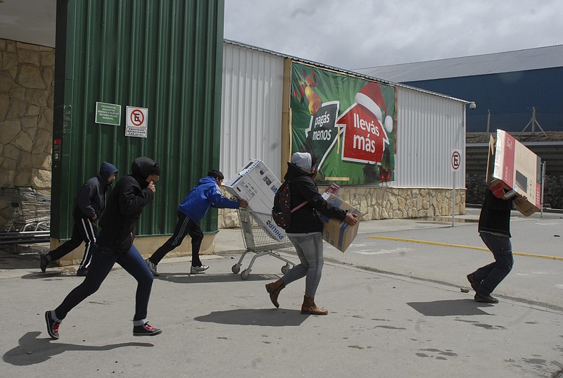 People run away carrying electronic goods Thursday during looting at a supermarket in San Carlos de Bariloche. The sign in the background reads in Spanish "pay less, take more."