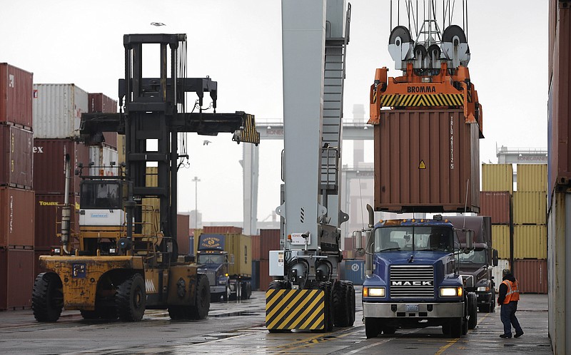 A truck driver watches as a freight container, right, is lowered onto a tractor trailer by a container crane at the Port of Boston in Boston. The crane and a reach stacker, left, are operated by longshoremen at the port. The longshoremen's union extended their contract Friday, averting a walkout by dock workers represented by the International Longshoremen's Association, would bring commerce to a near halt at ports from Boston to Houston.