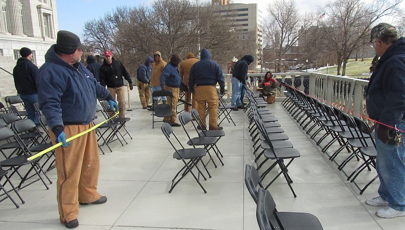 Workers from the state Division of Facilities Management use measuring tape to make sure the lines of chairs are evenly spaced for today's inauguration ceremony.                               