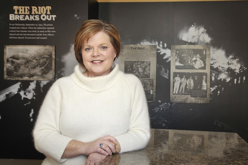 Diane Gillespie poses in front of a large mural of the 1954 riot, located in the second floor museum dedicated to the former Missouri State Penitentiary.