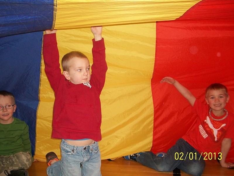 Eagle's Nest Preschoolers Aiden Evers and Ethan Wunderlich enjoy a physical education class, playing with a large parachute at Cole R-5 Schools in Eugene.