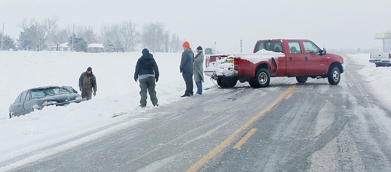 Benjamin Kramer, Holts Summit, in the orange hat, watches as a friend uses a log chain to pull Kramer's Chevrolet Cavailer from a ditch after it overturned Wednesday morning on U.S. 54. The car was pulled out on Route NN, an access road next to U.S. 54. Kramer said he lost control in slush after a semi truck passed him in the northbound lane of U.S. 54. 