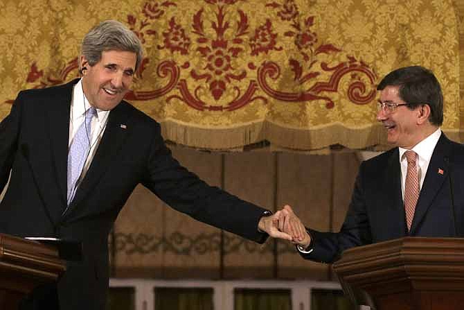 U.S. Secretary of State John Kerry leans over to clasp Turkish Foreign Minister Ahmet Davutoglu's hand on Friday at the end of a news conference at Ankara Palace in Ankara, Turkey. Ankara is the fifth leg of Kerry's first official overseas trip, a nine-day dash through Europe and the Middle East.