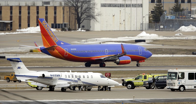 Emergency vehicles surround an aircraft, bottom, that sits on the tarmac Monday after making an emergency landing as another jet takes off at Lambert St. Louis International Airport in St. Louis. An official says the eight passengers aboard the small aircraft with landing gear troubles walked off the plane after it landed safely.