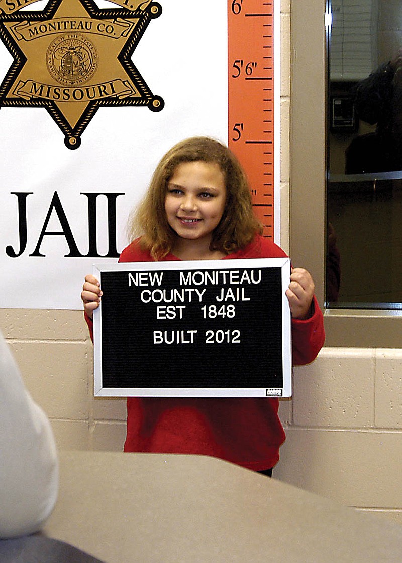 At the open house of the new Moniteau County Jail, KaLynn Irey poses with a sign in the place the booking photos are to be taken. 