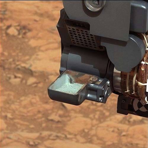 The Curiosity rover holds a scoop of powdered rock on Mars. The rover recently drilled into a Martian rock for the first time and transferred a pinch of powder to its instruments to analyze the chemical makeup.