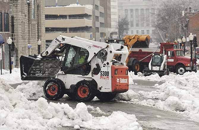 Street Department crews scoop snow piles away from the curb and haul it away by the truck load. One of the major cuts planned by the city is street chemicals, which largely pertain to snow removal. (File photo)