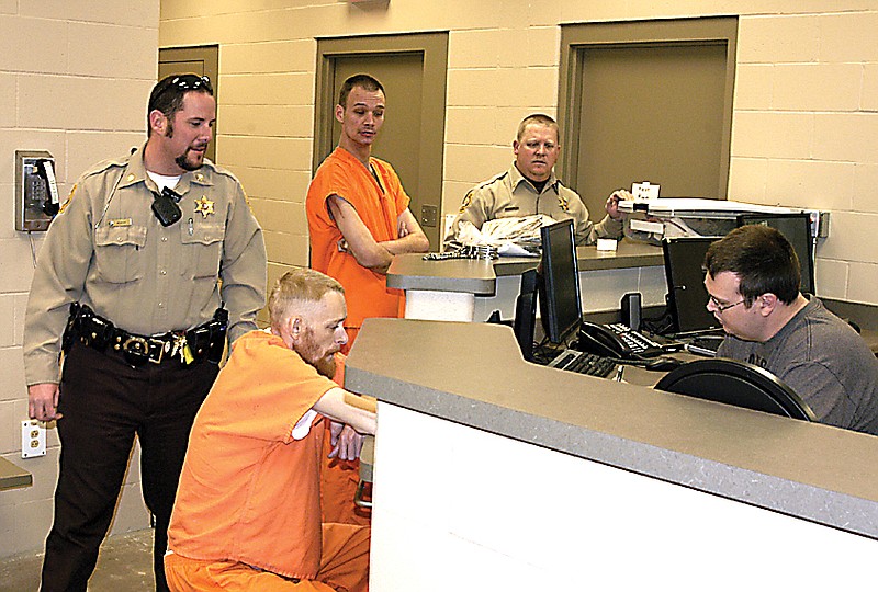 Reserve Jailer John Lucas, right, books the first two inmates to  transfer into the new jail from the old jail. Chief Deputy Kevin Morse, left, and Sheriff Jeptha Gump, far center, oversee the operation. 