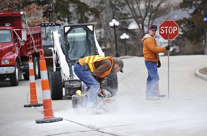 Johnny Braun holds the traffic sign as Adam Gaggens uses a power saw to cut concrete on Millbrook Drive. Crews from the Jefferson City Department of Public Works were busy recently filling potholes and repairing broken concrete around the city. 