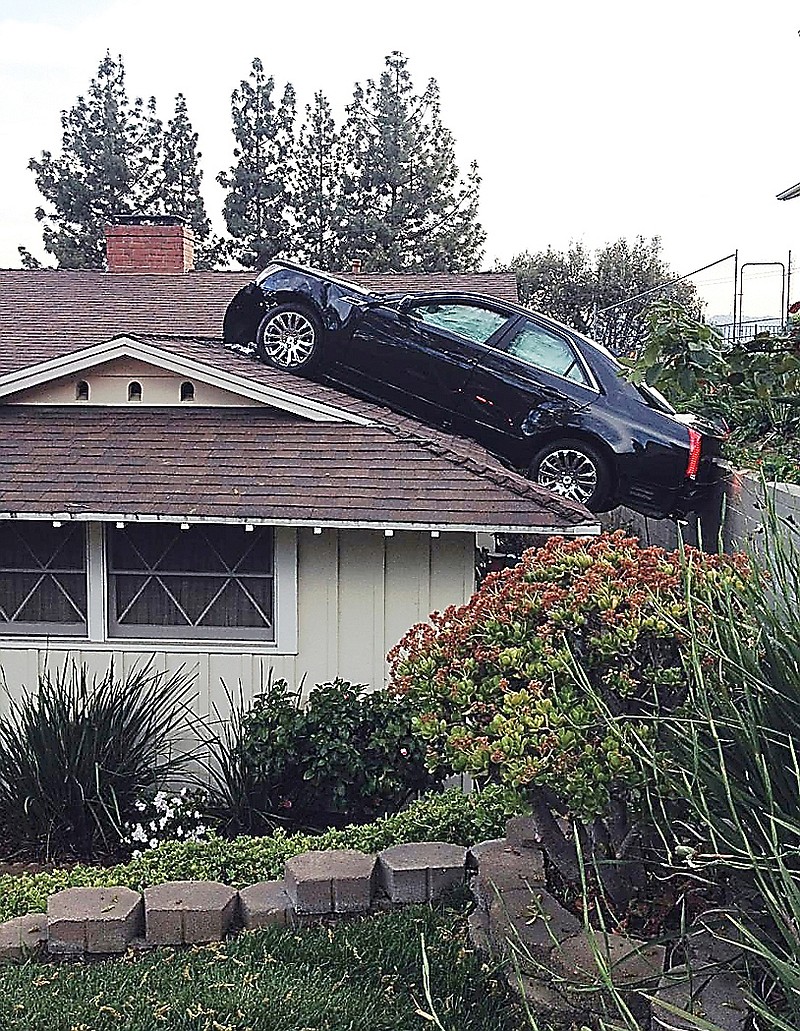 A Cadillac sits on a house roof after the driver lost control.