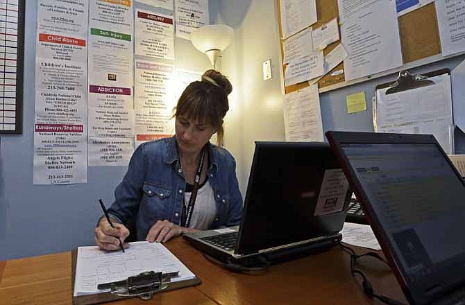 In this Tuesday, March 26, 2013 photo, Kara Hoppe, one of the adult supervisors, is seen with a wall full of help resources at the Teen Line center, that takes text messages and phone calls from teens seeking help, at Cedars Sinai Medical Center in Los Angeles. As more teens have gone mobile, using their phones as an extension of themselves, hotline providers have tried to keep up. Fewer seem to operate today than in decades past.