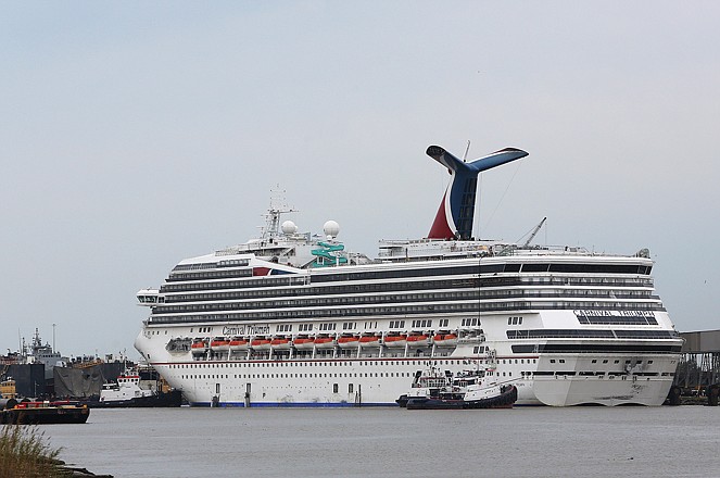 Tug boats maneuver around the Carnival cruise ship Triumph as it rests against a dock after becoming dislodged from its mooring at BAE Shipyard during high winds Wednesday. A worker at the dock who was thrown into the water at the same time is still missing, but authorities have called off the search for him.