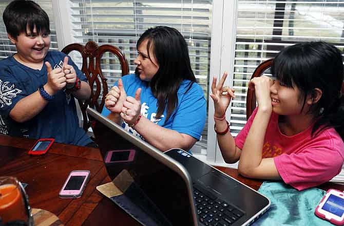In this April 4, 2013 photograph, Colton Smith, 10, left, uses a combination of some basic Chinese and English sign languages with his mother, Niki Smith, center, to communicate with their family's newest member, 14-year-old Guan Ya, in their Rienzi, Miss., home. Although the Smiths and their three other children are using the Google Translate program to communicate almost exclusively with Guan Ya, who is deaf, the children use a variety of signs as well. The family uses iPhones, iPods and a laptop, all loaded with the program to write in either English that translates to Chinese or vice versa. 