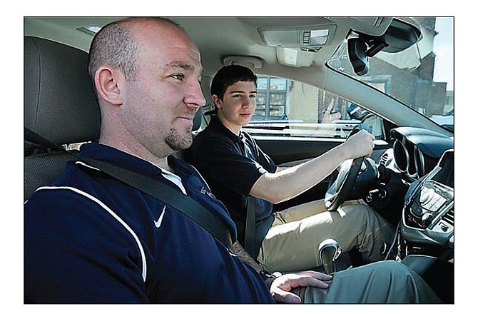 Helias Catholic High School freshman Alex Faddoul, seated in the driver's seat, checks the right mirror before pulling into Jefferson City traffic. Seated in the passenger seat is instructor Travis Reinsch.