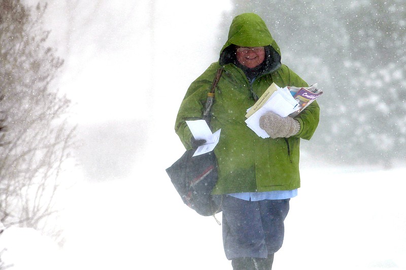 U.S. Postal Service carrier Nancy Schmidt walks along Ninth Street in Rapid City, S.D. on Tuesday afternoon after an early spring storm hit with rain, thunder, heavy snow and strong winds. 
