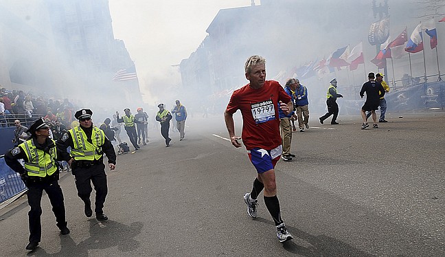 A Boston Marathon competitor and Boston police run from the area of an explosion Monday near the finish line in Boston.