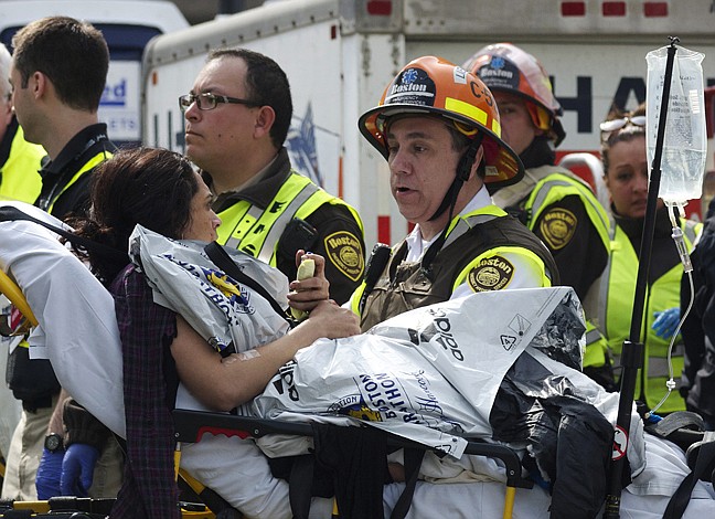 Emergency responders comfort a woman on a stretcher who was injured in a bomb blast near the finish line of the Boston Marathon Monday, April 15, 2013 in Boston. Two bombs exploded in the packed streets near the finish line of the marathon on Monday, killing at least two people and injuring more than 80, authorities said. 