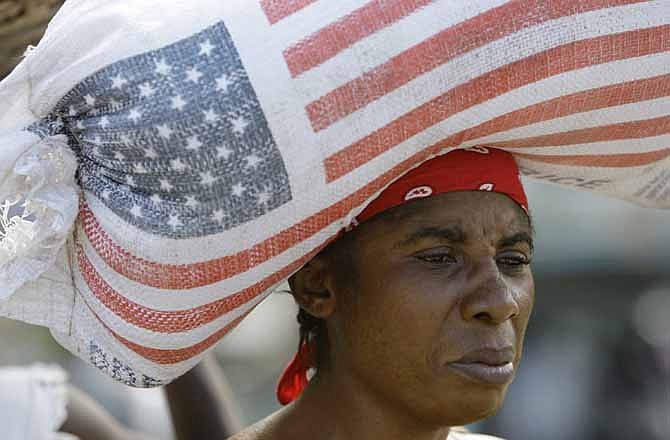 In this Jan. 16, 2010, file photo, a woman carries a bag containing rice donated by the United States Agency for International Development, USAID, as she walks through a market in Leogane, Haiti, days after a powerful earthquake hit Haiti. Food aid groups are pushing President Barack Obama's administration to overhaul the way the United States helps starving people abroad. At issue is whether the government should ship U.S.-grown food overseas to aid developing countries and starving people or simply help those countries with cash to buy food. Currently, the United States is shipping food abroad, a process many food aid groups say is inefficient.