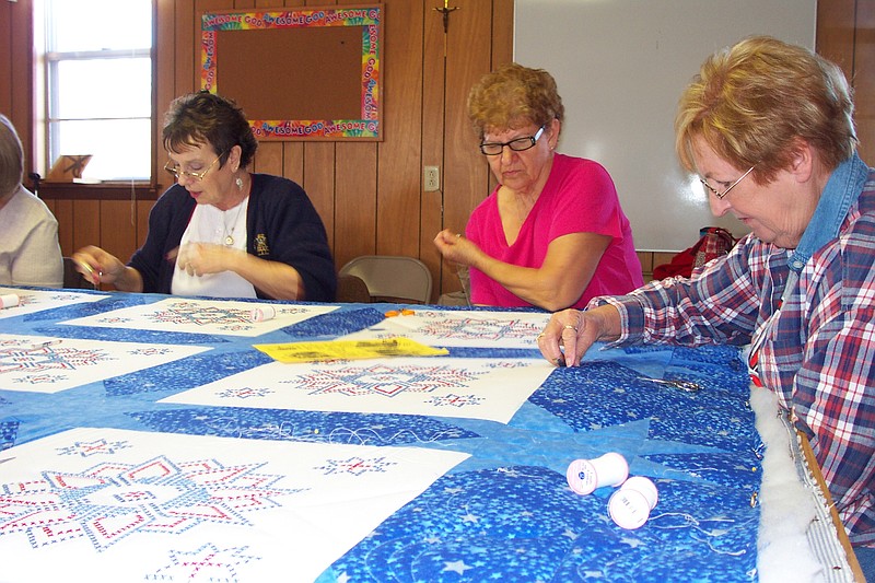 Sharon Murphy, Burt Koestner and Grace Kallenbach add their stitching to this patriotic quilt, which will be auctioned at the Russellville 175th anniversary celebration in June. Nearly two dozen ladies from the Russellville area have taken turns quilting the blanket this month. 