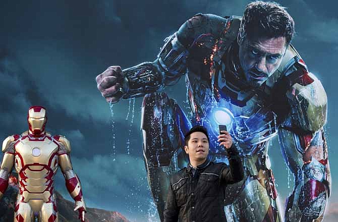 In this April 6, 2013 file photo, a Chinese man uses a smartphone to take his own photo with an "Iron Man" poster together with a costumed figure, left, during a promotional event of the new movie "Iron Man 3" at the Imperial Ancestral Temple in Beijing's Forbidden City. From demanding changes in plot lines that denigrate the Chinese leadership, to dampening lurid depictions of sex and violence, Beijing is having increasing success in pressuring Hollywood into deleting movie content Beijing finds objectionable.