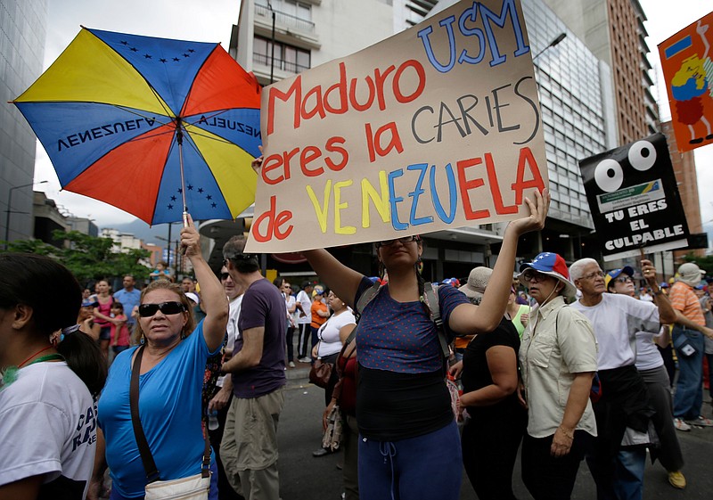 An opposition protester holds up a poster Wednesday that reads in Spanish "Maduro you are the cavity of Venezuela" during an opposition May Day march in Caracas, Venezuela.  Venezuelans filled the streets of the capital in rival marches by the opposition and the government less than a day after a brawl on the floor of congress injured several opposition lawmakers. 