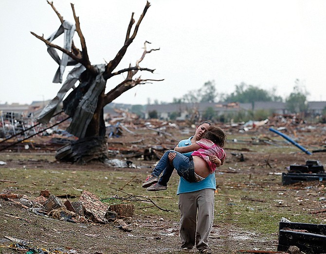 A woman carries a child through a field near the collapsed Plaza Towers Elementary School in Moore, Okla.