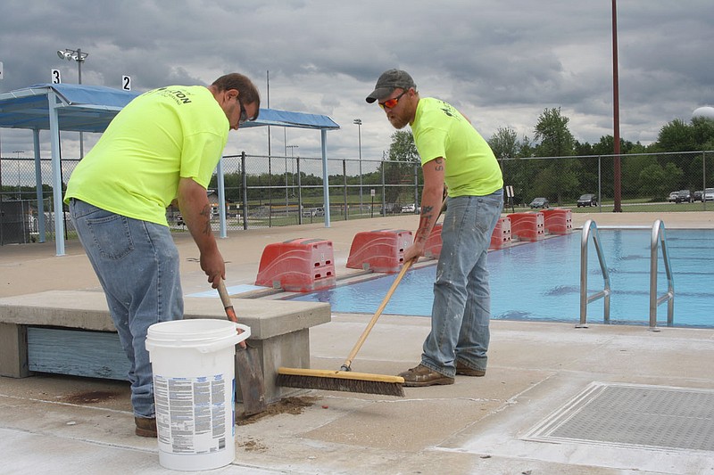 (From left) Andrew Wieschhaus and Scott Pace work to prepare the Oestreich Swimming Pool for opening, sealing cracks in the deck. Fulton's city pool opens at noon on Saturday.