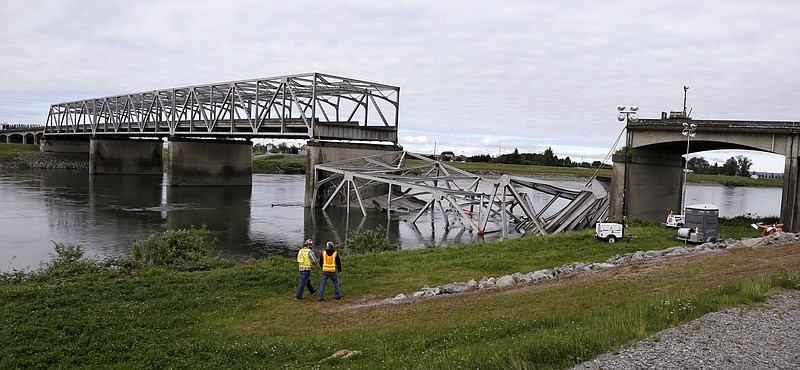 Workers walk past the collapsed portion of the Interstate 5 bridge Friday at the Skagit River in Mount Vernon, Wash. A truck carrying an oversize load struck the four-lane bridge on the major thoroughfare between Seattle and Canada, sending a section of the span and two vehicles into the Skagit River below Thursday evening.