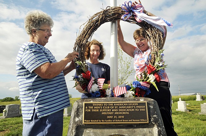 Janet Koetting, left, Marilyn Daledovich and Judy Hoelscher hold and fasten the large wreath to the flagpole in the Veterans Memorial at St. Margaret's Cemetery. Volunteers from the community of Osage Bend have worked to raise money to improve the cemetery and to decorate veterans' graves.