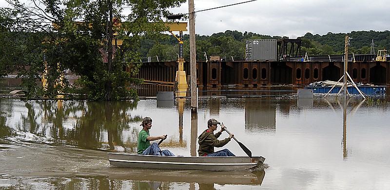 Curtis and Adam Strope paddle through Osage River floodwaters Sunday as they pass the $20 million railroad bridge being built across the river. Some of the materials for the project were underwater. 
