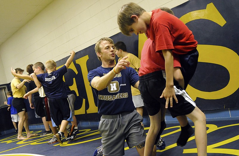 New Helias wrestling coach Jacob Wadley gives some pointers to Jared Schulte (left) and Jase Dummel as the pair of campers work on a takedown exercise Monday during the Crusaders' youth summer wrestling camp at Rackers Fieldhouse.