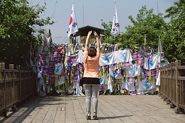 A visitor stands on her toes while taking souvenir photos in front of a wire fence covered with ribbons carrying messages left by visitors wishing for the reunification of the two Koreas.