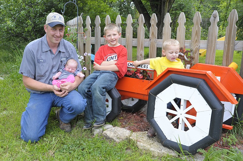 CUTLINE FATHERS DAY: Greg Holtgrewe holds his newborn daughter Adrian next to an Allis-Chalmers replica tractor flower box with his sons Garret, 6, and Grant, 3. Holtgrewe enjoys sharing his love of farm life with his family, including wife Amanda. Democrat photo/Michelle Brooks
