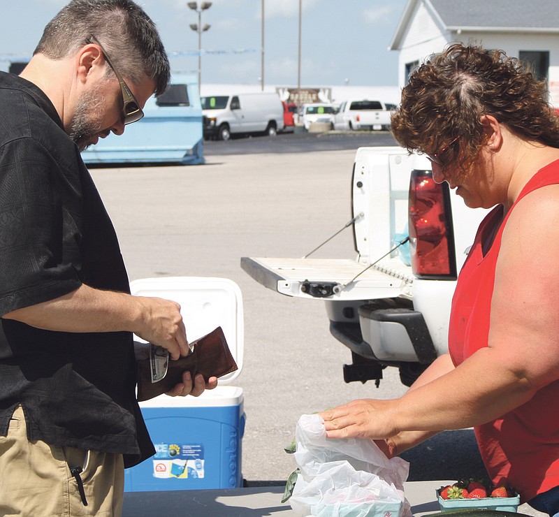 David Brett of Fulton pays for produce as vendor Joan Schwede bags fresh strawberries and broccoli Wednesday afternoon in the parking lot at Sutherland's on U.S. Business 54 in Fulton.