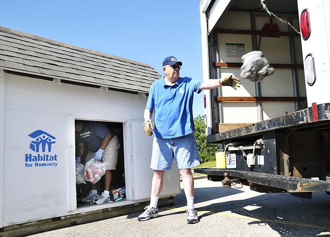 Gary Penny stands inside the can cottage and hands bags of aluminum cans to John Yovich to toss into the box truck on Wednesday. Volunteering for Habitat for Humanity and using his personal truck, Yovich started picking up the cans 10 years ago and a few years later graduated to the enclosed truck. Penny has been helping with this project for three years. There are several collection spots around Jefferson City and surrounding communities and over the years, enough money has been raised to build one home.