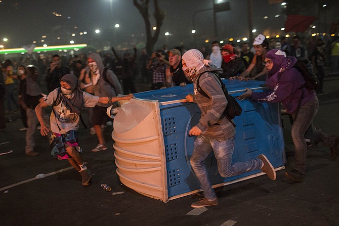 Protesters drag a portable toilet to add to a burning barricade during an anti-government demonstration Thursday in Rio de Janeiro, Brazil. Police and protesters fought in the streets into the early hours Friday in the biggest demonstrations yet against a government viewed as corrupt at all levels and unresponsive to its people. 