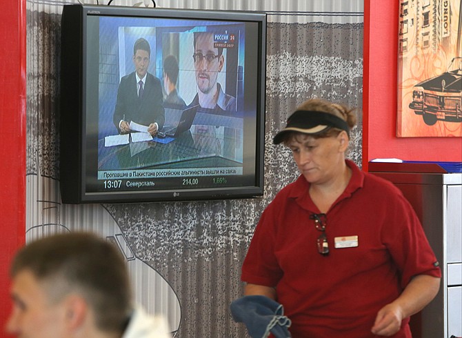 An airport worker passes a TV screen with a news program showing a report Wednesday on Edward Snowden at Sheremetyevo airport in Moscow. Russia's President Vladimir Putin said Tuesday that National Security Agency leaker Edward Snowden has remained in Sheremetyevo's transit zone, but media that descended on the airport in the search for him couldn't locate him there.