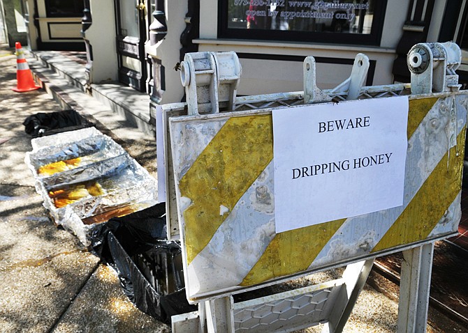 Two bees inspect a sign downtown warning passersby to beware their handiwork, which drips into the pans on the sidewalk. Honey is dripping from a hive or hives in a decorative enclosure of the building on East High Street that houses G2 Gallery and the Missouri Trucking Association. 