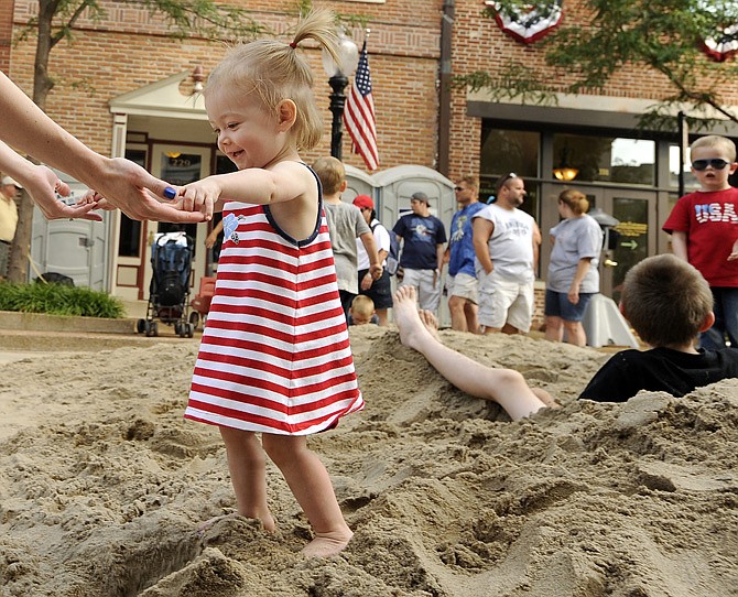 Lucy Veile takes her mom Sarah Veile's hands and makes her way out of the sand as she and dozens of other children enjoy playing in the Madison Street sand lot during the Salute to America festival's Independence Day celebration on Thursday.
