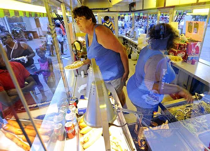 Bunita Rainke, left, of Southern Fun Carnival waits to hand a customer a freshly fried funnel cake while working at the Missouri American Water Carnival Land's Madison Street food stand during Jefferson City's Salute to America on Wednesday evening, July 3, 2013.