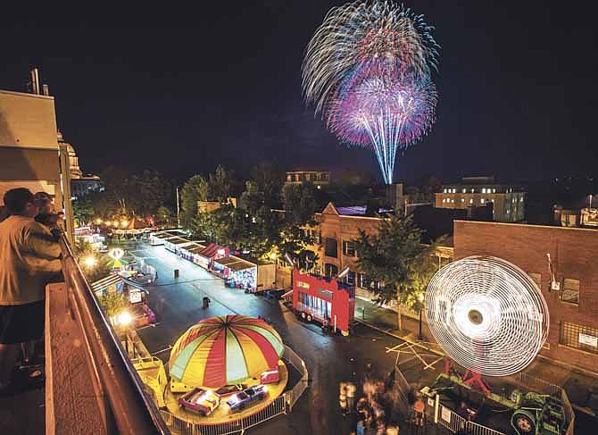 Spectators look out from the City Parking Garage over the spinning carnival rides filling Jefferson City's Capitol Avenue as fireworks light up the sky during the grand finale of the Missouri Credit Union "Red White and Boom!" fireworks display at the conclusion of the two-day Salute to America on Thursday, July 4, 2015.